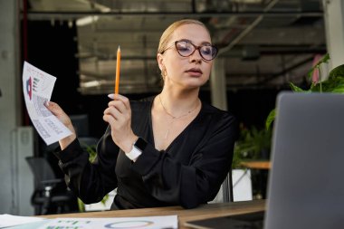 A dedicated young plus size woman reviews documents while sitting at her workstation. clipart