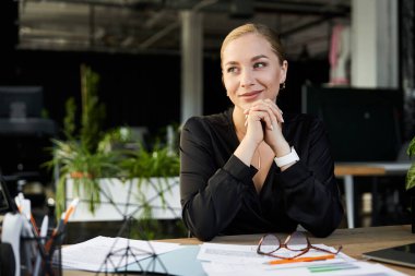 A young plus size woman in a stylish black outfit contemplates her work amidst vibrant greenery. clipart