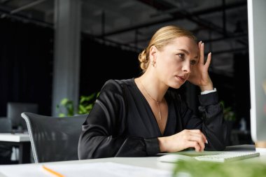 Genç ve iri yarı bir kadın, görevleri hakkında derin düşüncelere dalmış, çalışma masasına dikkatle odaklanır..