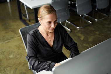 A plus size young woman diligently works at her computer in a contemporary office setting. clipart