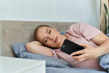 Genç, güzel, iri yarı bir kadın yatağında rahat bir şekilde uzanıyor, telefonuna dalmış..