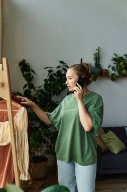 Genç ve kilolu bir kadın evde telefonla sohbet ederken kıyafetlerini seçiyor..