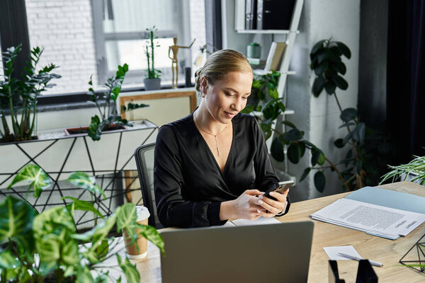Молодая, красивая, плюс размер женщина сосредоточена на своем телефоне во время работы в стильном офисе.