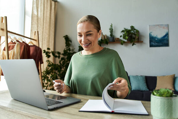 A cheerful young plus size woman engages with her laptop, showcasing a vibrant home workspace.