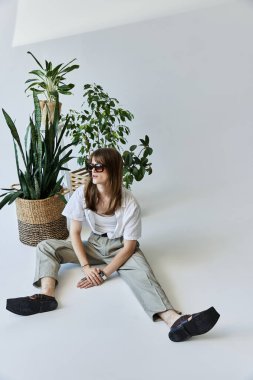 A stylish young man lounges on the floor, surrounded by vibrant indoor plants. clipart