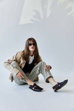 Genç bir adam modaya uygun giysiler içinde rahatlar. Minimalist bir arka planda yaratıcılık ve tarz yayar..