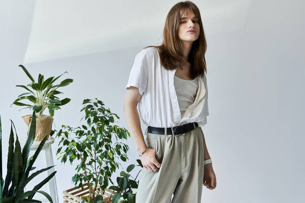 Stylish young man posing in fashionable attire surrounded by potted plants in a modern space.
