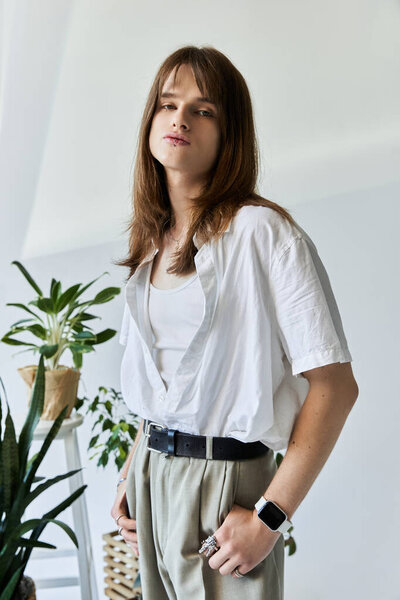 A trendy young man poses confidently in casual yet fashionable attire surrounded by greenery.