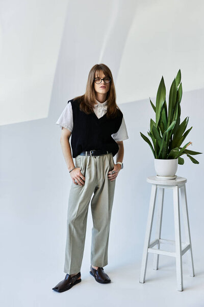 Модный молодой человек уверенно позирует в стильной одежде рядом с декоративным растением.