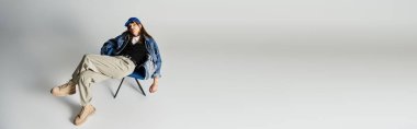 Moda kıyafetleri içinde genç bir adam bir sandalyede serinliyor, modern moda ve kendine güveni somutlaştırıyor..