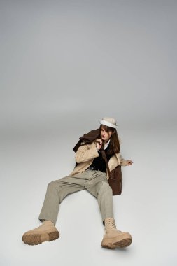 Genç bir adam yerde oturuyor ve modaya uygun kıyafetlerini sanatsal bir şekilde sergiliyor..