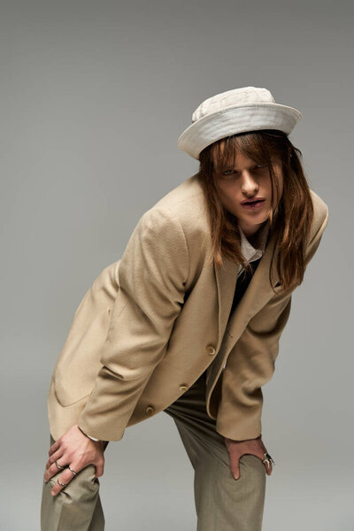 Молодой стильный человек игриво наклоняется, излучая уверенность в модном, расслабленном наряде.