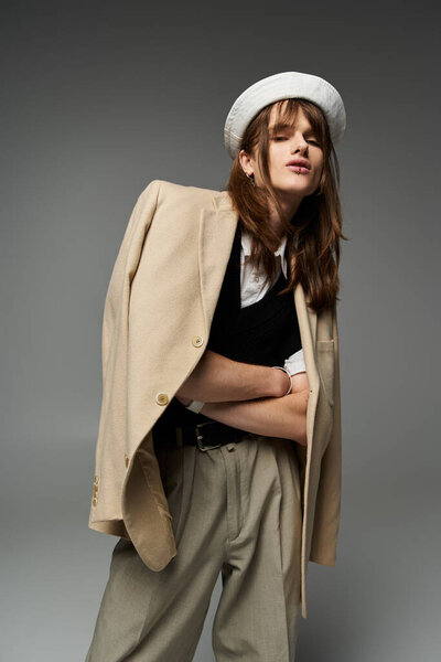 Молодой человек, одетый в модный костюм, занимает уверенную позу на нейтральном фоне..