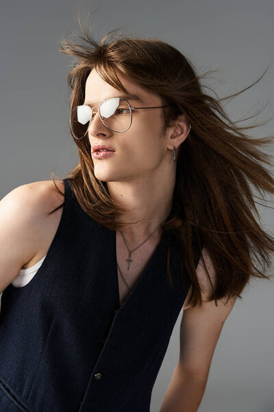 Модный молодой человек с длинными волосами уверенно позирует в стильных солнцезащитных очках.