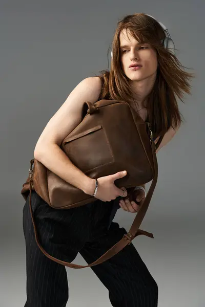 stock image This young man showcases a fashionable outfit while confidently holding a brown bag.