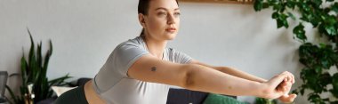 Genç, sportif bir kadın, spor kıyafetleriyle egzersiz yapıyor, ev antrenmanının keyfini çıkarıyor..
