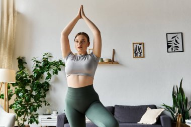 Sportif bir kadın, rahat oturma odasında yoga pozu veriyor. Forma ve farkındalığa odaklanıyor..