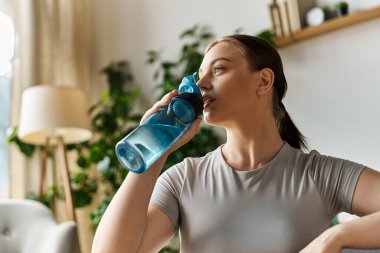 Aktif çalışan genç bir kadın yoğun bir ev çalışmasından sonra hidrat tüketiyor, fitness hedeflerini destekliyor..