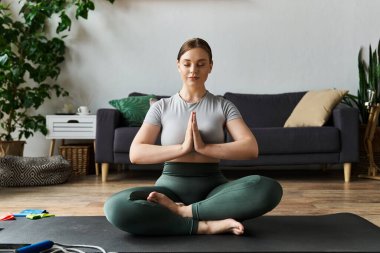 Genç bir kadın evde yoga yapıyor. Etrafı bitkilerle çevriliyken meditasyon pozisyonunda oturuyor..