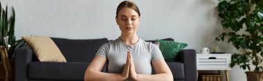 Kendini işine adamış genç bir kadın rahat oturma odasında yoga yapıyor. Farkındalığı ve zindeliği kucaklıyor..