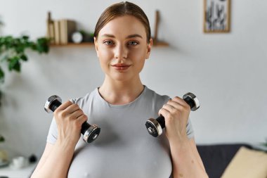 Kendini işine adamış genç bir kadın, modaya uygun spor kıyafetleri içinde ağırlık kaldırıyor..