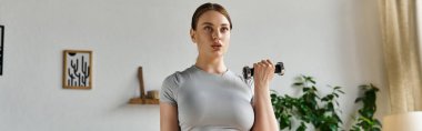 Genç ve sportif bir kadın evde spor yapıyor. Aktif şık kıyafetler giyerken spor yapmaya odaklanıyor..
