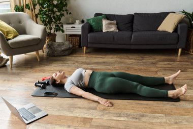 Genç bir kadın, sıcak ve davetkar bir yaşam alanıyla çevrili bir antremandan sonra yoga minderinde dinleniyor..