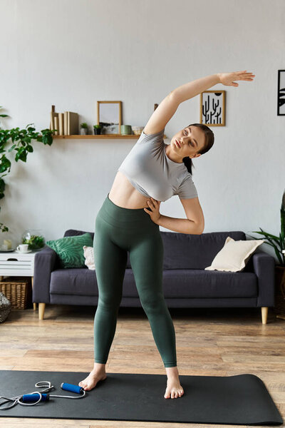 Молодая спортивная женщина растягивается дома, одетая в топ и леггинсы, обнимает фитнес и велнес.