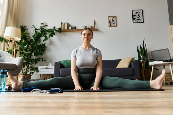 Молодая спортивно одетая женщина практикует свои растяжки на коврике для йоги в уютной домашней обстановке.