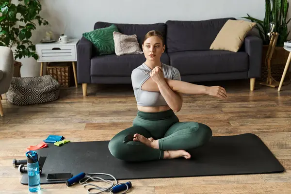 stock image A sportive woman exercises at home, engaging in a workout while stretching on a yoga mat.