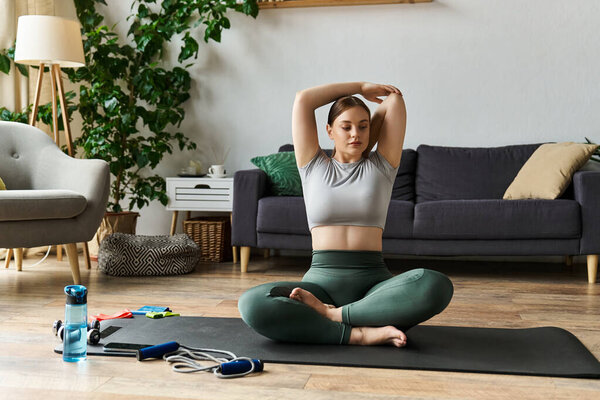 Молодая спортивная женщина растягивается, сидя на коврике для йоги в своем стильном доме, полностью занятая в своей тренировке.