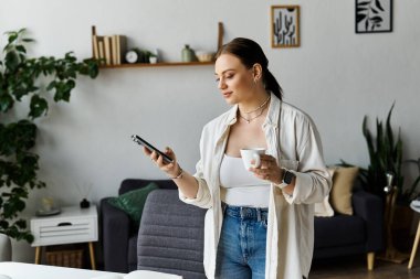 Genç bir kadın evden çalışırken telefon ve kahve arasındaki zamanını dengeliyor..