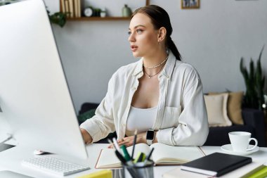 A dedicated young woman works at her home office, immersed in tasks on her large computer monitor. clipart