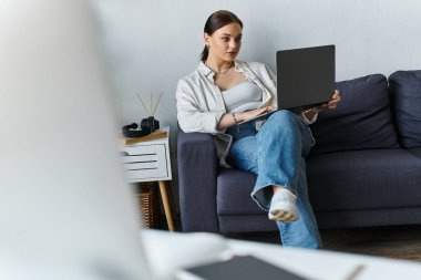 Amidst a cozy home setting, a young woman works intently on her laptop, embodying remote productivity. clipart