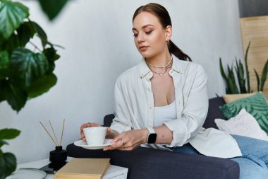 Günlük kıyafetli genç bir kadın evde kahve yudumluyor..