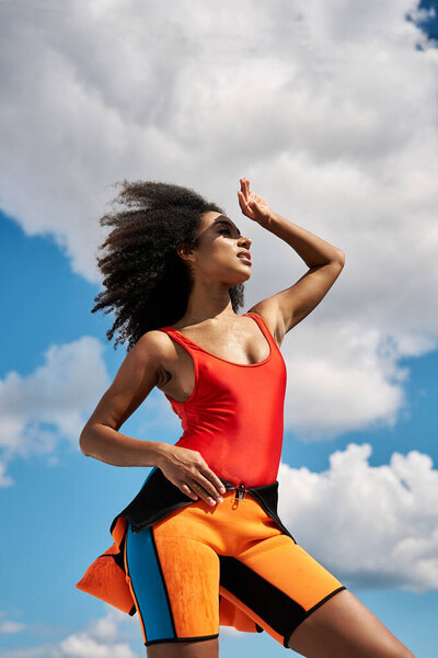 A stylish young woman poses confidently against a backdrop of vibrant blue skies and fluffy clouds.
