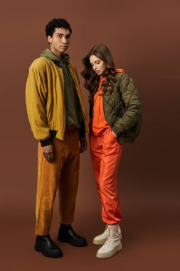 A stylish couple dressed in autumn attire poses against a cozy brown background. clipart