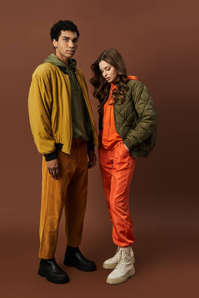 Стильная пара в осеннем наряде позирует на уютном коричневом фоне.