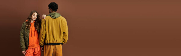 A stylish young couple flaunts unique autumn fashion, exuding confidence against a warm backdrop.