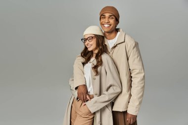 Şık bir çift neşeli poz verir, canlı sonbahar kıyafetlerini yumuşak bir arka planda sergilerler..