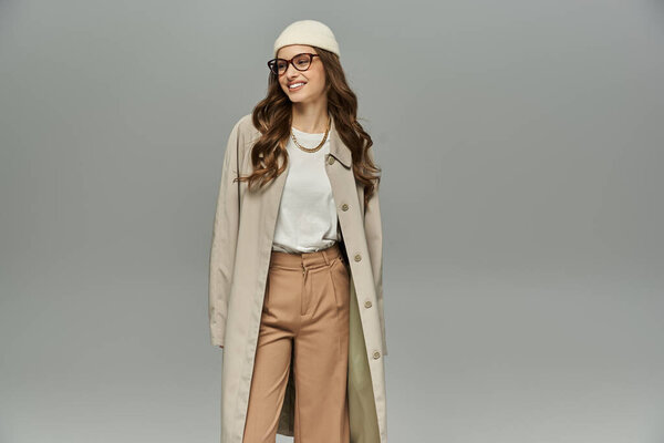 Привлекательная женщина в элегантном осеннем наряде позирует на сером фоне.