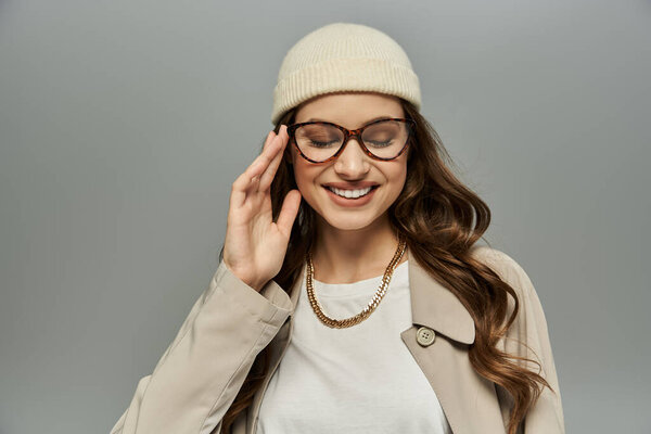 Элегантная женщина в элегантном осеннем наряде позирует на сером фоне.