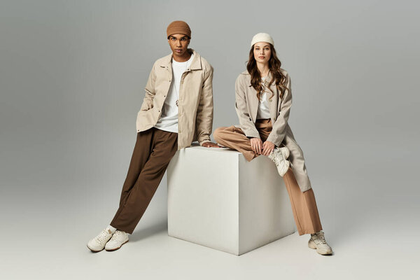 A stylish couple expresses their unique autumn fashion against a minimalist backdrop.