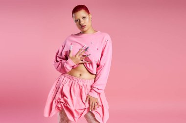 The young woman in the studio confidently poses, showcasing her vibrant pink hair and unique fashion choice. clipart