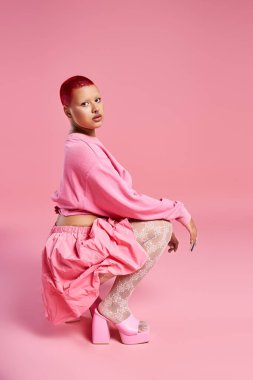 Pembe saçları olan genç bir kadın, eşsiz moda anlayışını, neşeli bir stüdyo ortamında sergiliyor..