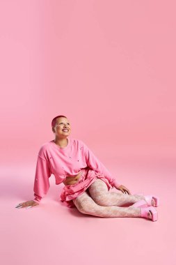 Yumuşak pembeyle süslenmiş bir stüdyoda, kısa pembe saçlı genç bir kadın eşsiz moda anlayışını sergiliyor..