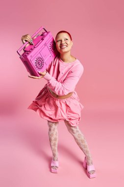 Pembe saçlı yaratıcı genç bir kadın elinde canlı bir aksesuar tutarken eşsiz tarzını neşeyle sergiliyor..