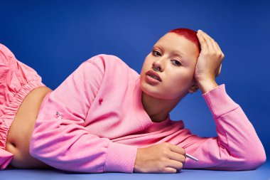 Pembe saçlı, kendine güvenen genç bir kadın stüdyo ortamında kendine has moda anlayışını sergiliyor..