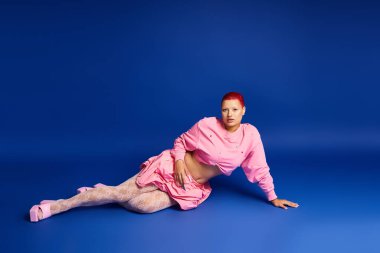 Pembe elbiseli genç bir kadın dikkat çekici bir mavi arka plana karşı, kendine güvenle uzanır..