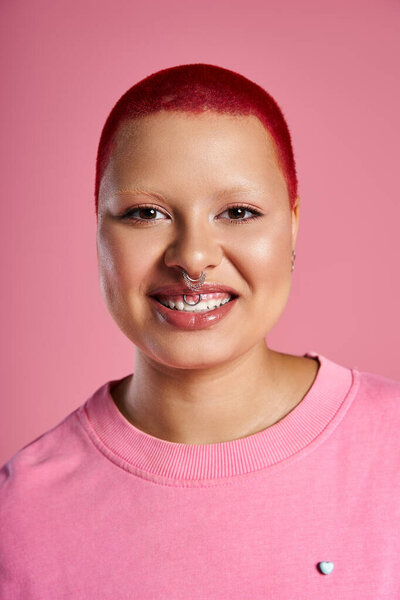 Showcasing vibrant style, a young woman with short pink hair and a nose piercing smilghtly.